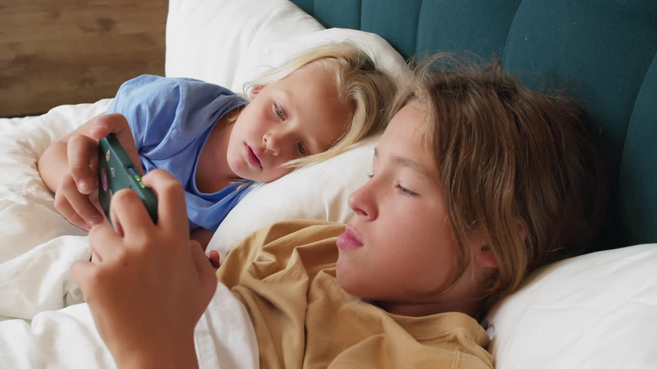 아이들이 침대에서 스마트폰으로 놀고 있습니다.