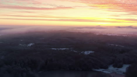 misty forest on snowy lake shore at golden hour sunset