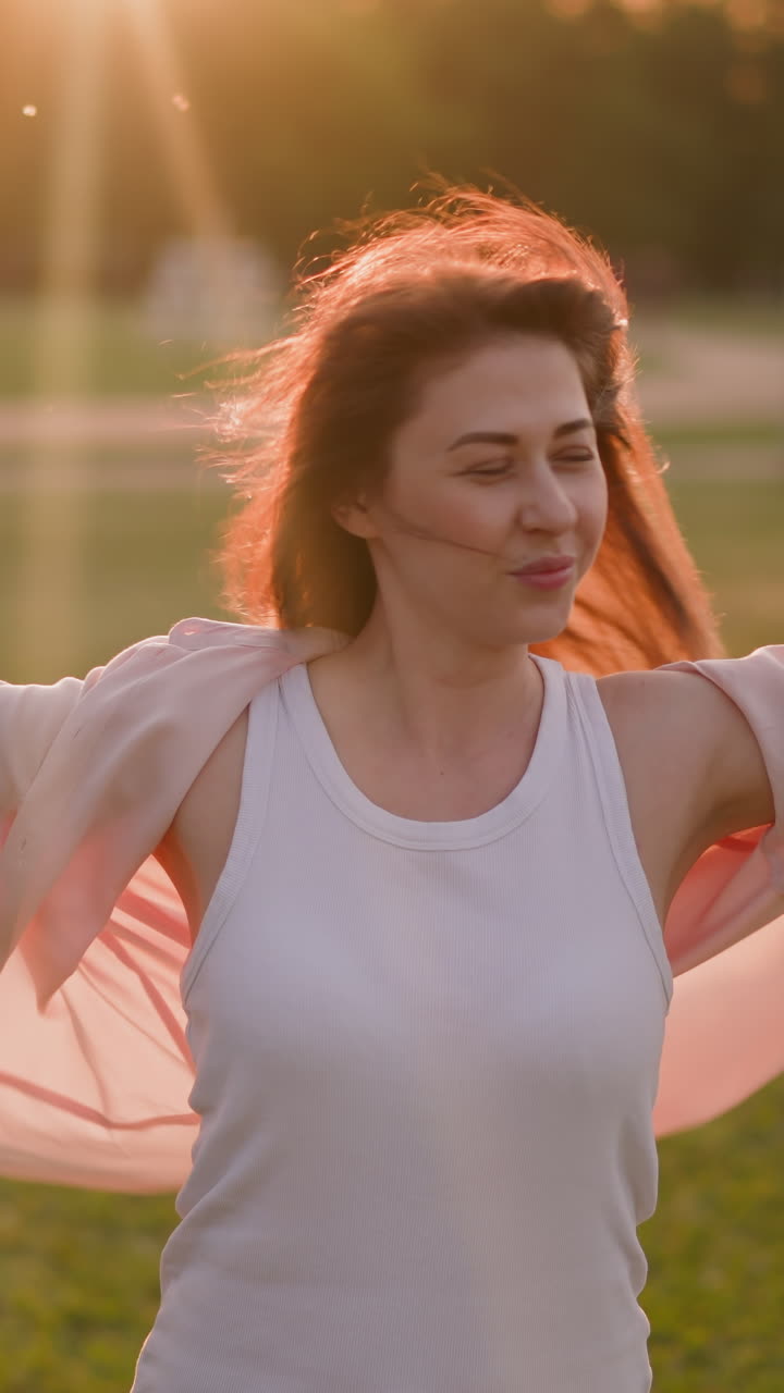 Positive woman raises hands enjoying strong wind on meadow at sunset slow motion. Inspiring summer weather. Lady spends time in park