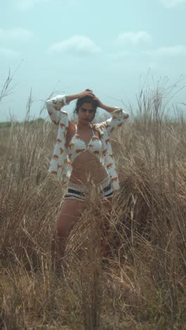 a young woman in a field of tall dry grass, posing in a stylish outfit under clear skies