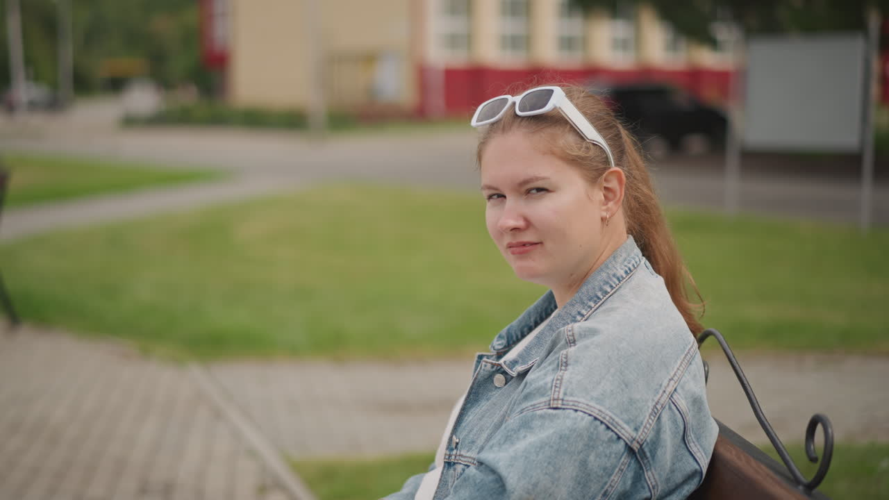 Nuori valkoinen nainen istuu penkillä opiskelemassa muistikirjaa, reppu vieressään. Taustalla on kivetty aukio ja kaupunkirakennuksia. Hänellä on yllään farkkutakki ja lenkkarit, ja hän katsoo vilpittömästi kameraan keskittyneen opiskelutauon aikana.