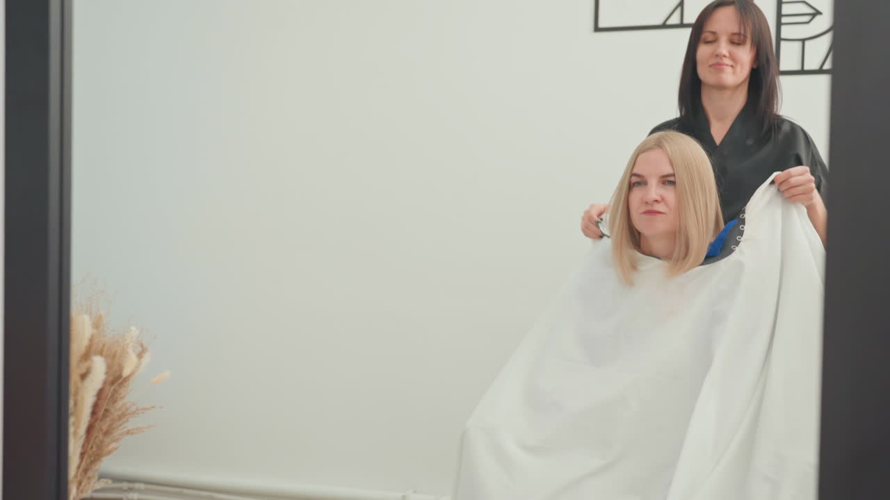 La capa revela un cambio de estilo y una transformación inminentes; el cliente espera ansiosamente un nuevo peinado y un nuevo aspecto; el equipo de estilistas se prepara mientras la capa indica un cambio de estilo y una renovación inminentes.