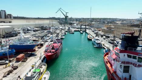 drone aéreo disparado volando lento y bajo sobre el mar azul entre varios barcos y barcos en un patio de barcos muy ocupado