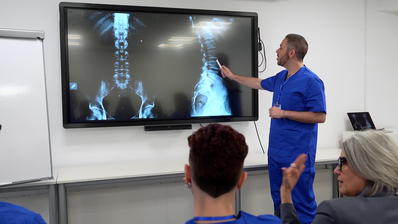 Medico che presenta radiografie della colonna vertebrale a studenti di medicina in un'aula.