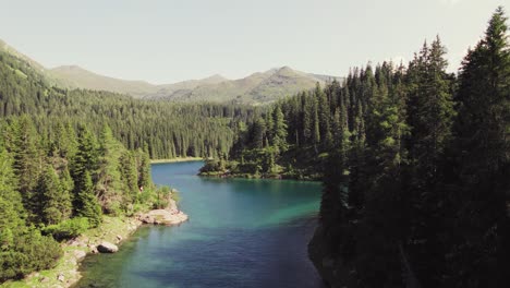 cinematic drone aerial rising over a beautiful alpine mountain lake surrounded by woods and mountain peaks