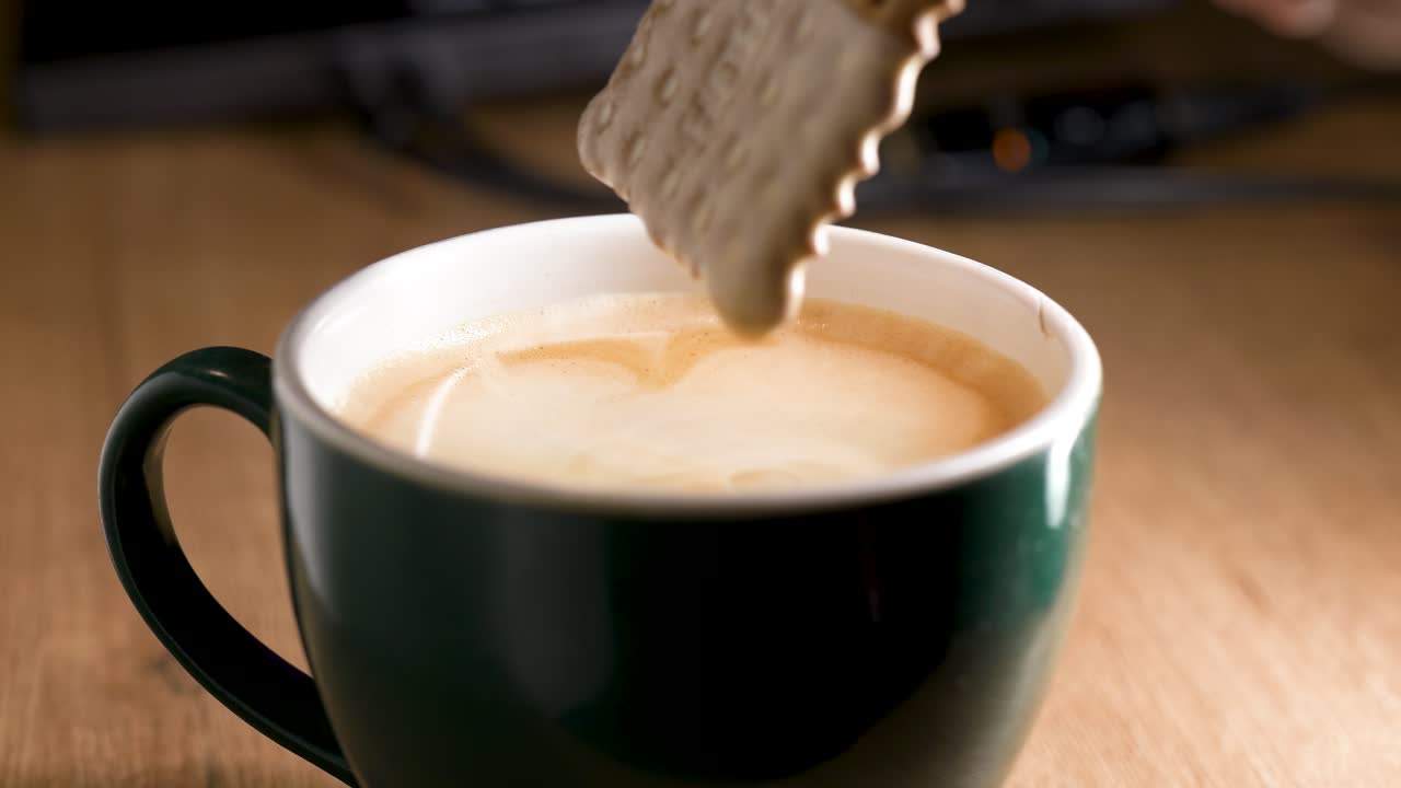 Dettaglio di un biscotto immerso in una tazza di caffè bollente su una superficie di legno. Un concetto di stile di vita accogliente legato alle pause caffè, al relax e al comfort.