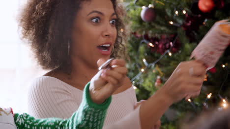 young black woman sitting at christmas dinner pulling crackers with her multi generation family, close up