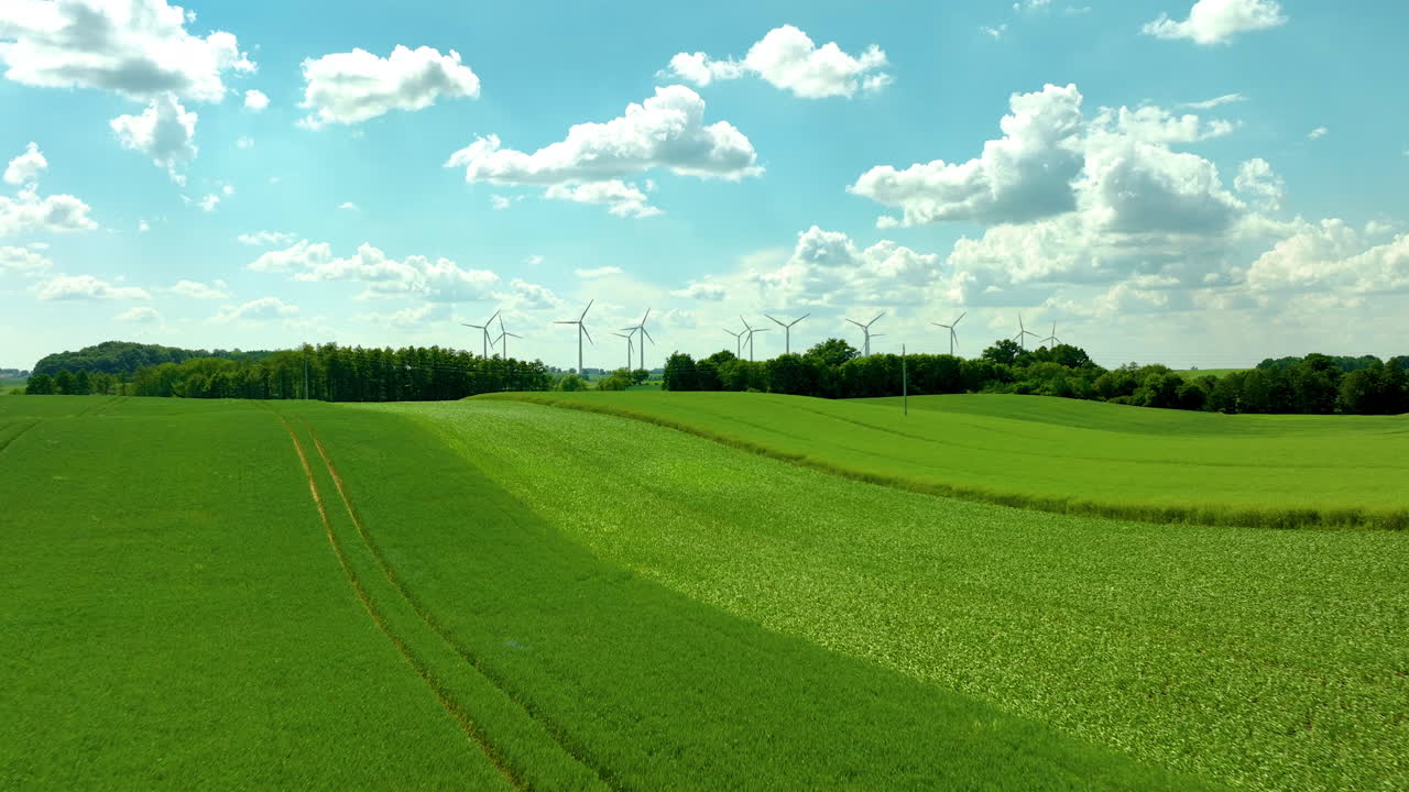 Aerial shot of green fields with wind turbines, bright blue sky, and scattered clouds - forward