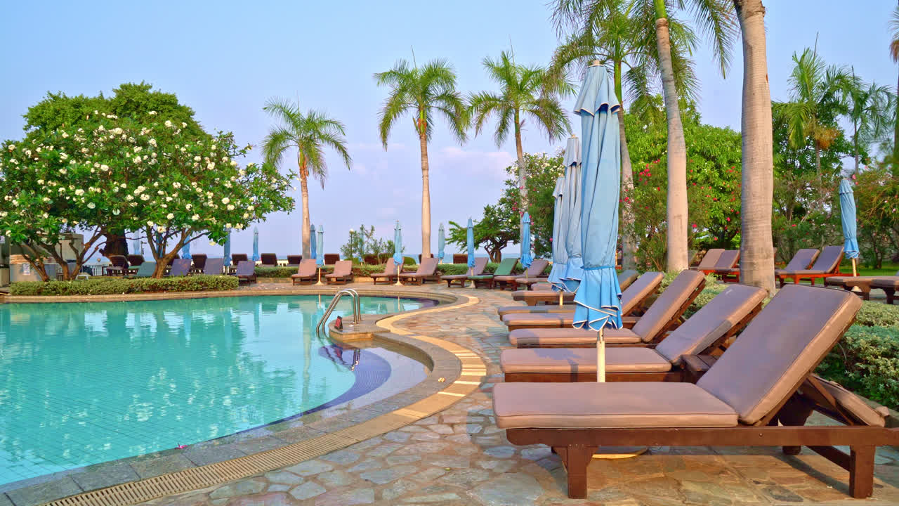 바다를 배경으로 한 수영장 주변의 의자 수영장 또는 침대 수영장과 우산 - 휴일 및 휴가 개념