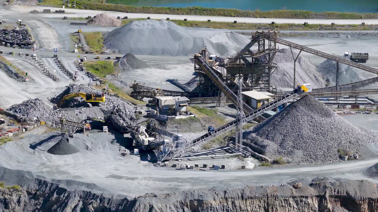 Drone footage captures an active quarry with machinery and vehicles under bright daylight, highlighting industrial mining activities