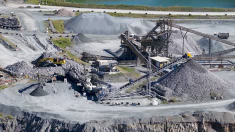 drone footage captures an active quarry with machinery and vehicles under bright daylight, highlighting industrial mining activities