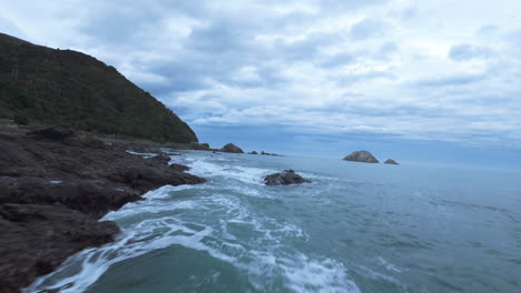fpv drone shot of the rocky coast of goosebay, gloomy evening in new zealand
