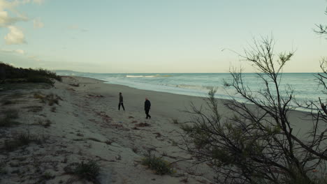 on a deserted winter beach two men walk while observing the sea stormy waves