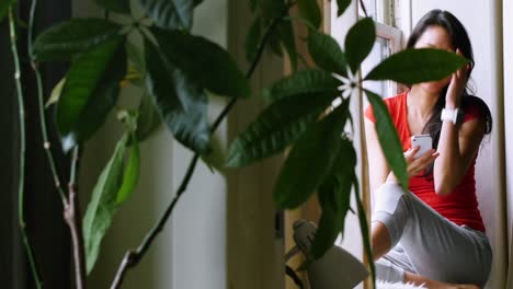 Woman-sitting-on-windowsill-and-using-mobile-phone