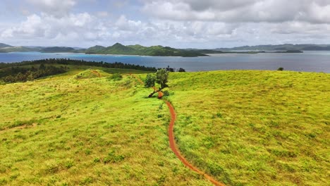 aerial landscape of corregidor island in siargao, philippines showing golden grassy hills, a red dirt path, distant forest, and the calm blue sea meeting scattered islets