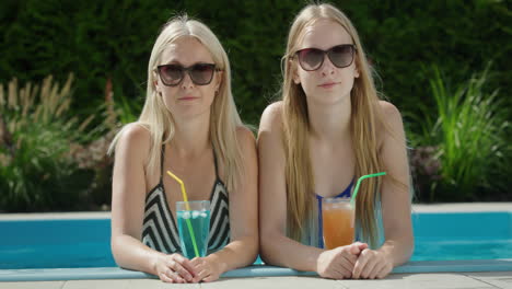 portrait of a mother with a teenage daughter. together they relax in the pool, drink refreshing cocktails.