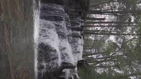 Toma-Vertical-De-Una-Impresionante-Cascada-Que-Cae-Sobre-Rocas-En-El-Bosque-En-Cámara-Lenta