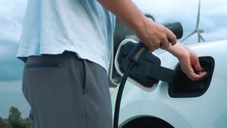 el hombre progresista carga su coche eléctrico con energía limpia generada por la turbina eólica.