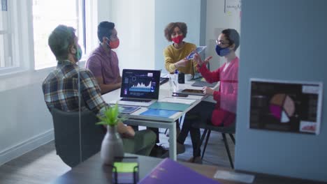 diversos colegas con máscaras faciales trabajando juntos en la sala de reuniones de una oficina moderna