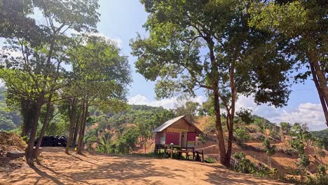 A tranquil scene of a red bungalow surrounded by lush greenery and trees under a clear blue sky in Phuket, Thailand