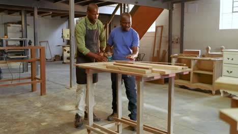african american mentor pointing guiding apprentice measuring wood with tape marking cuts at shop