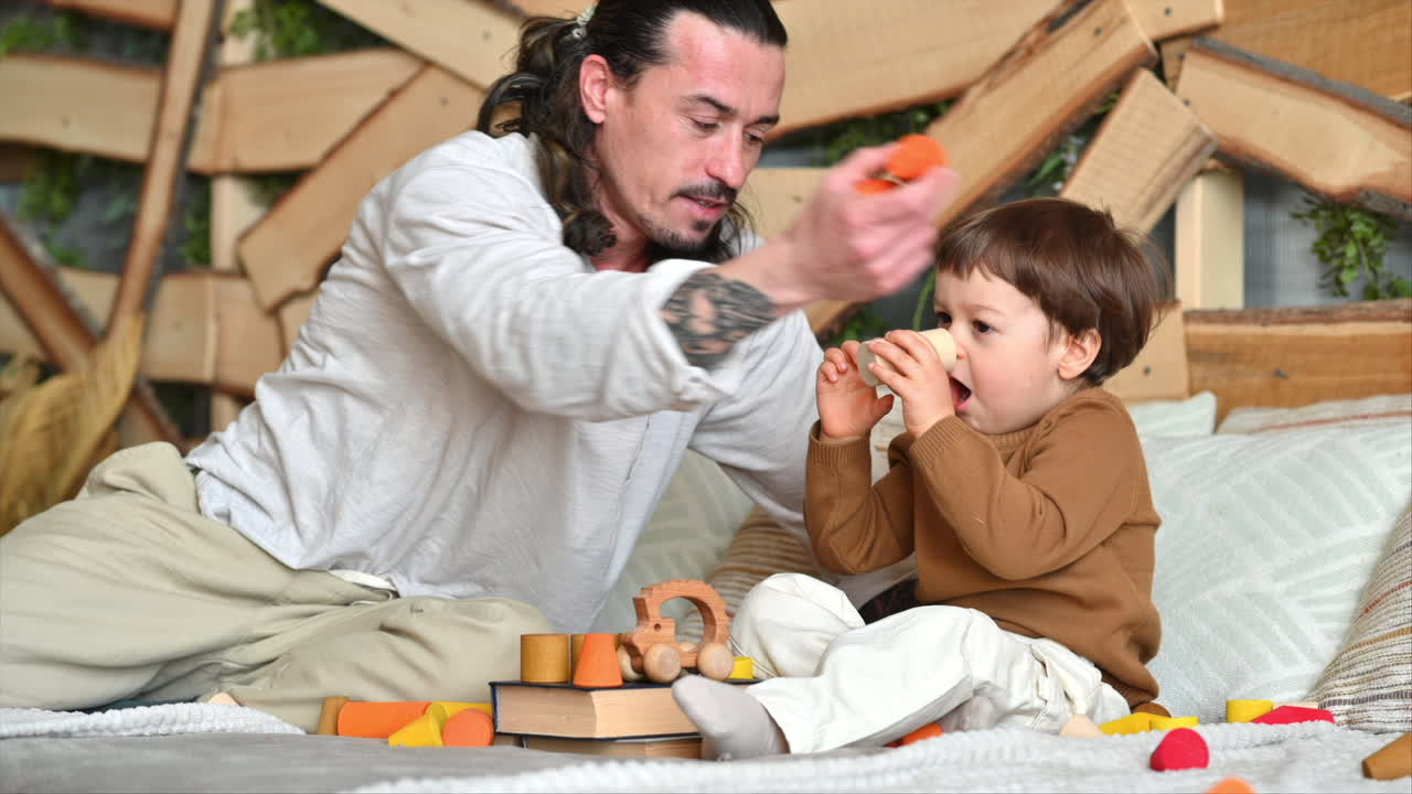 Father playing with his son with colourful, ecological wooden toys on the bed