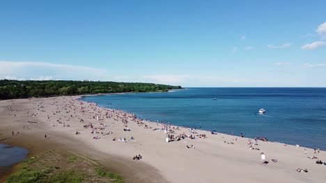 Toma-Aérea-De-Una-Concurrida-Playa-De-Toronto-En-Un-Día-Soleado-De-Verano-Con-Botes-En-El-Agua-Del-Lago-Ontario