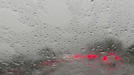 pouring rain over windscreen and red blurred lights of car traffic in background with wiper cleaning windshield from raindrops