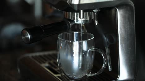 hombre girando un interruptor en una máquina de espresso automática para verter agua caliente humeante en una taza de vidrio transparente