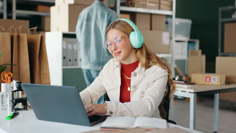 Woman with headphones working on laptop in a home office setting
