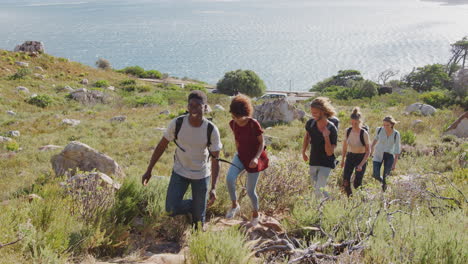 group of young friends hiking up cliffs on coastal path through countryside together