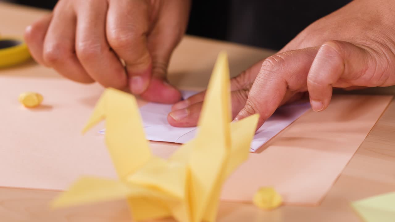 Close-up shot of hands carefully folding purple paper into an origami crane on a desk