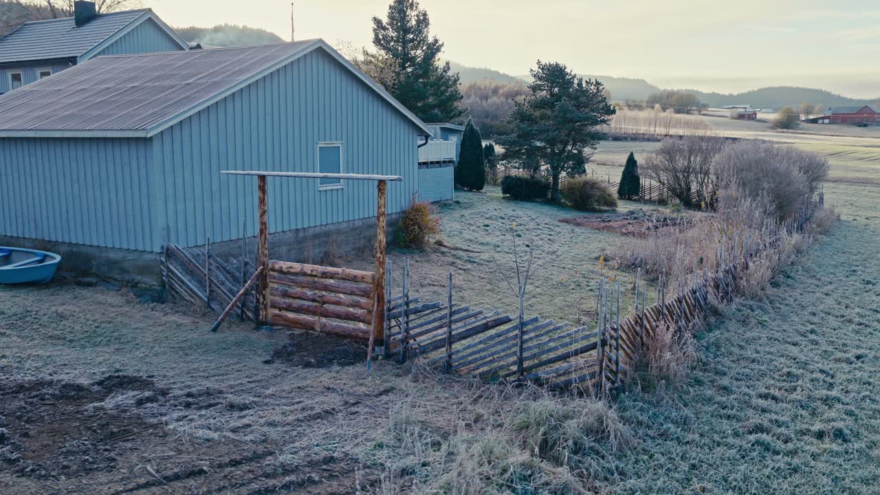 A Frost-covered Yard Lies Beside a Light Blue House and Rustic Fence - Orbit Drone Shot