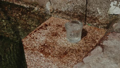 Close up of a glass being filled with clear water from a stone fountain