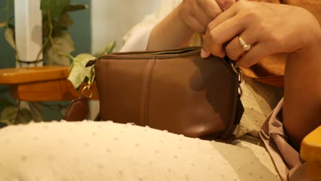 woman opening a brown leather shoulder bag