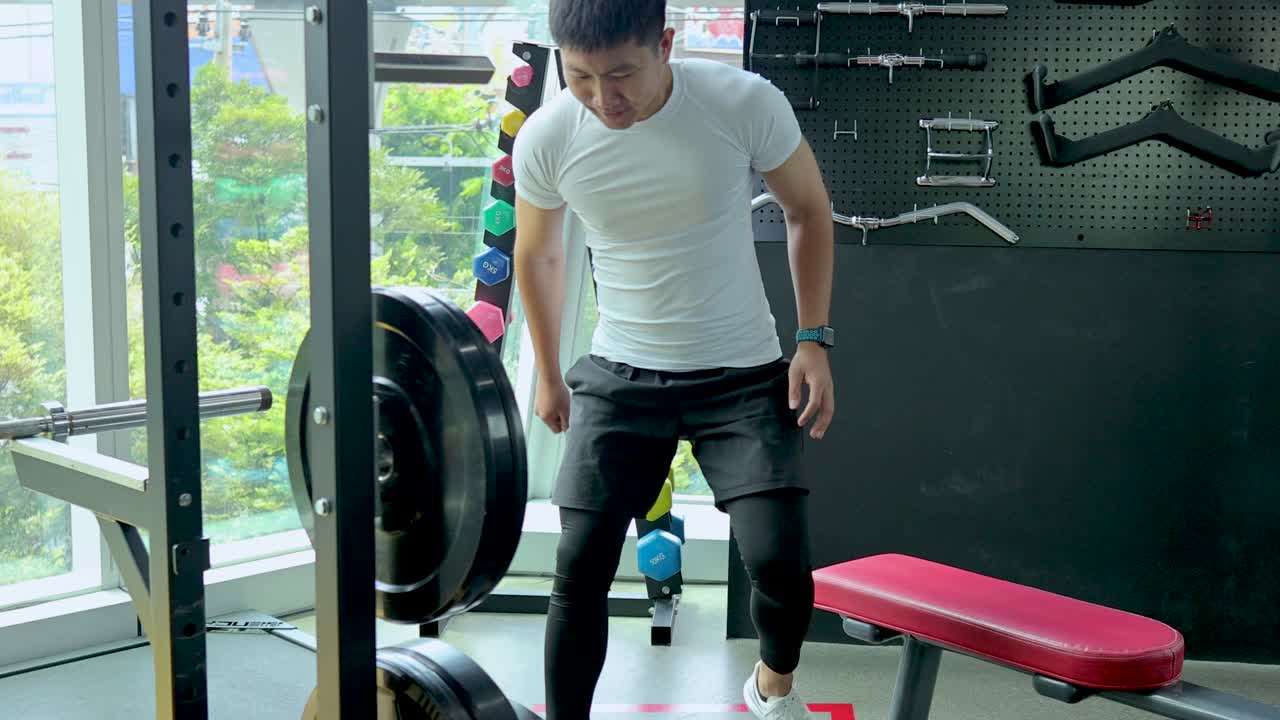 Athletic man adjusts barbell weights in bright gym, natural daylight, static camera, focused mood