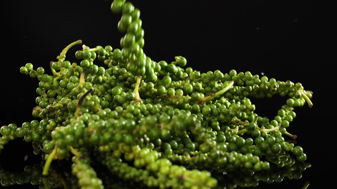 Green peppercorns cascade onto a glossy black surface, creating a vibrant and dynamic visual effect