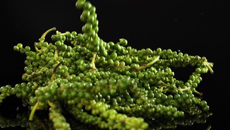 green peppercorns cascade onto a glossy black surface, creating a vibrant and dynamic visual effect