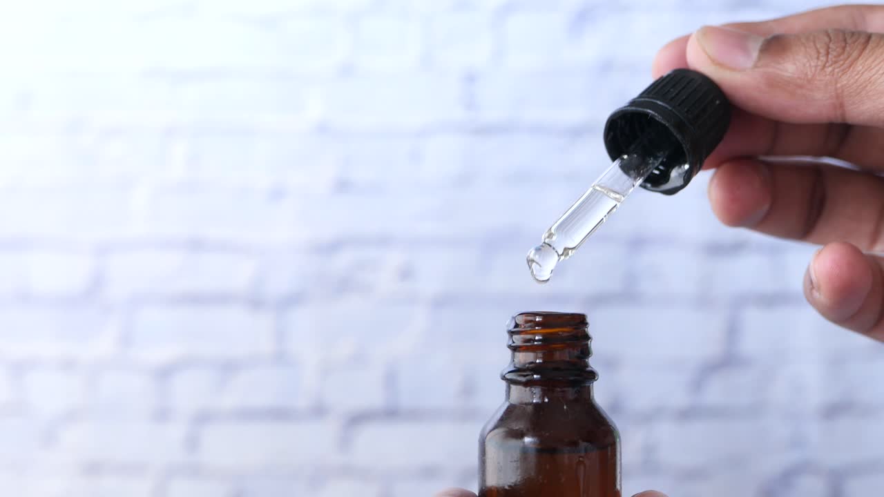 el gotero de la mano vertiendo líquido en una botella marrón