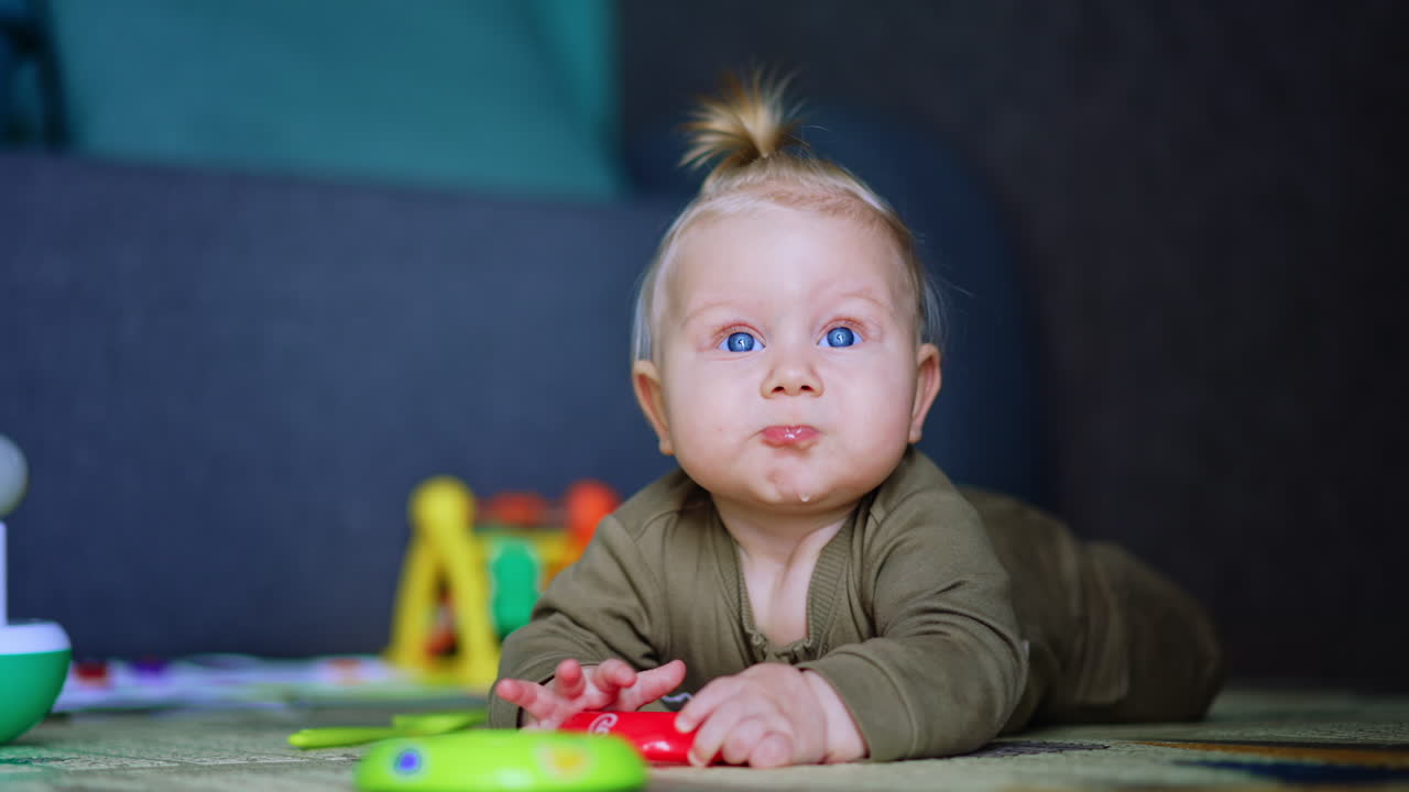 Adorable chubby infant boy lies on the floor. Kid crawls up and grabs one of the toys. Close up. Blurred backdrop.