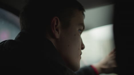 back view of road traveler making precise turn on busy city street, side profile shows focused male driver rotating steering wheel, blurred traffic lights and vehicles passing urban window