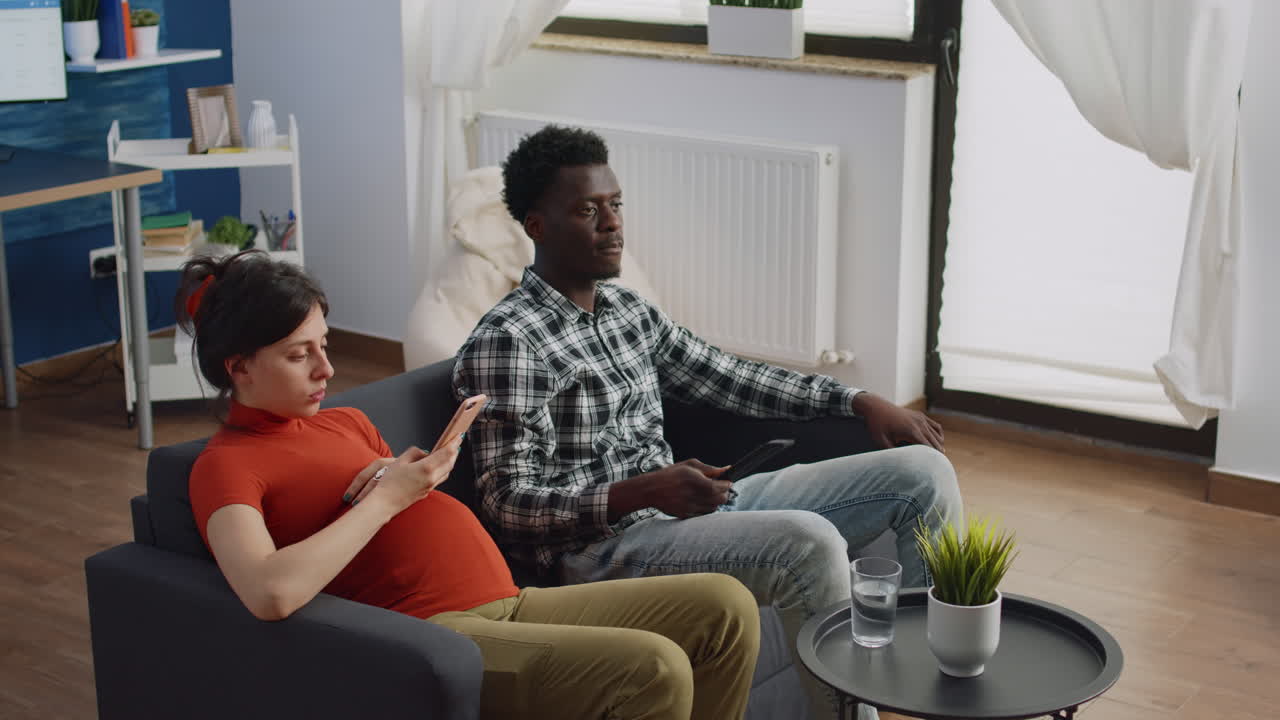 Interracial parents sitting in living room expecting child