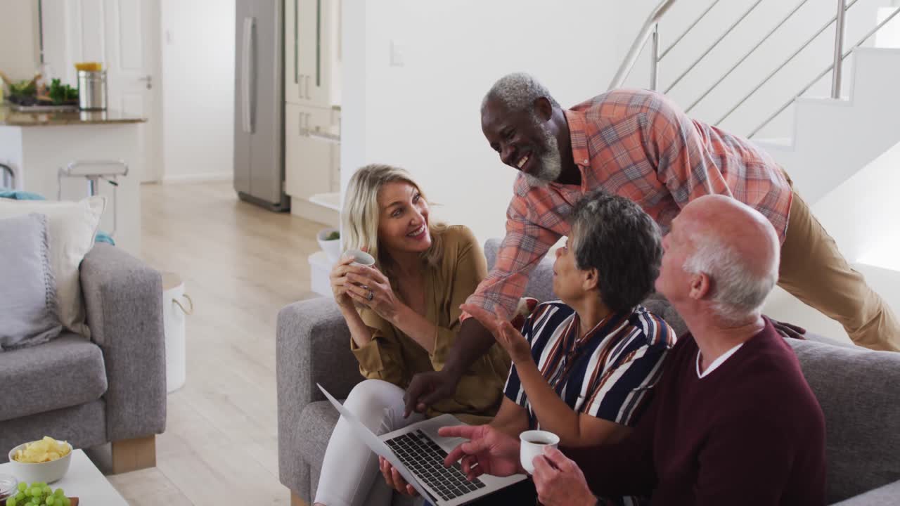 dos parejas mayores diversas sentadas en un sofá usando una computadora portátil y riendo