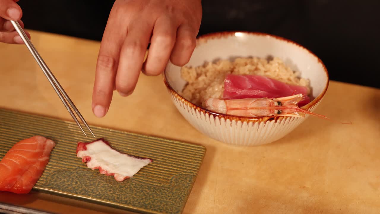 En kokk bruker spisepinner til å arrangere fersk sashimi og reker over en skål med ris.