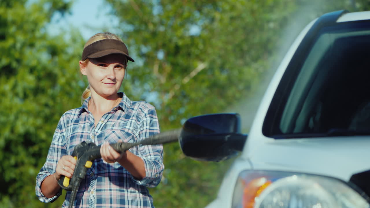 mujer joven lavando su auto cerca del garaje del patio trasero de la casa