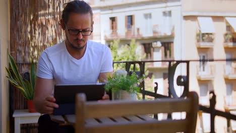 Attractive-Young-Millennial-Man-starts-Video-Call-zoom-conversation-Using-Tablet-Waving-chatting-exterior-balcony-apartment-during-sunny-summer-day-medium-shot