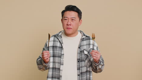 hungry asian man waiting for serving dinner meal dishes with restlessness holding cutlery fork knife