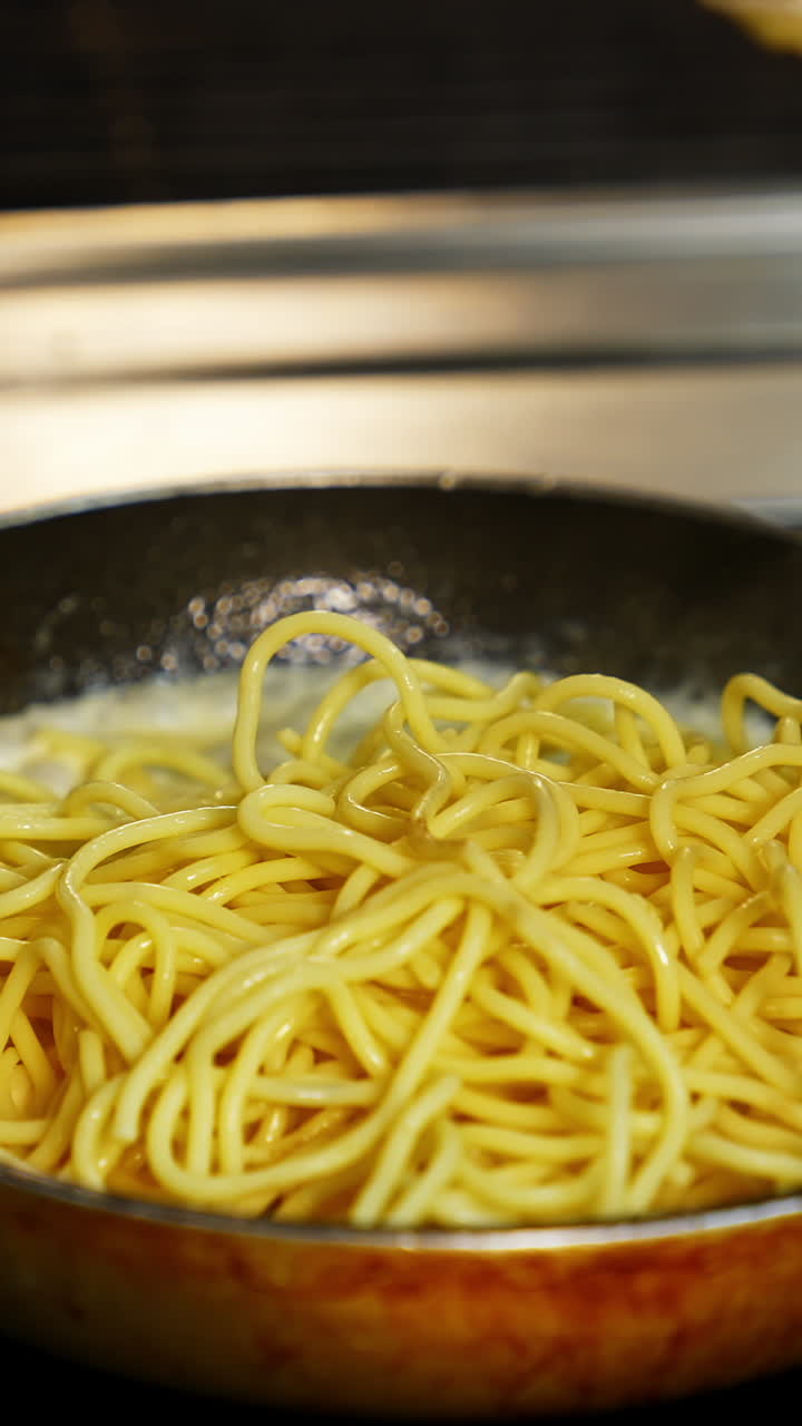 Man in white gloves puts spaghetti on a pan with white sauce. Bechamel in frying pan with pasta. Delicious dish video. Vertical video