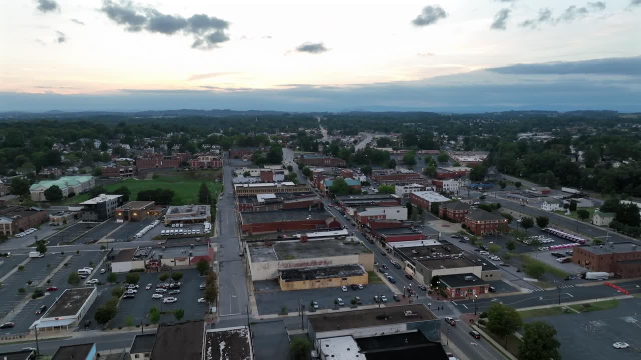 Drone flyover American city at sunset time. Traffic on Main Street along Shopping street. Parking area and historic houses in town. Clouds at sky in summer. Dusk scene. Wide shot