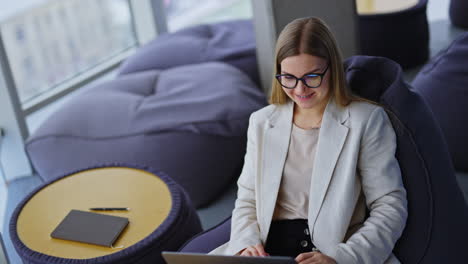 pleasant-looking woman in glasses leans back and sits comfortably in bean bag chair with laptop on her legs. modern office work concept.